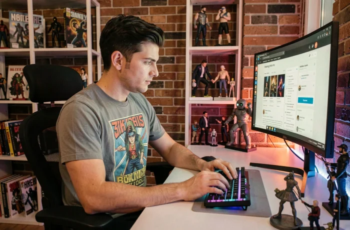 Jeune homme passionné de culture geek naviguant sur un forum en ligne entouré de figurines et de jeux vidéo dans son appartement